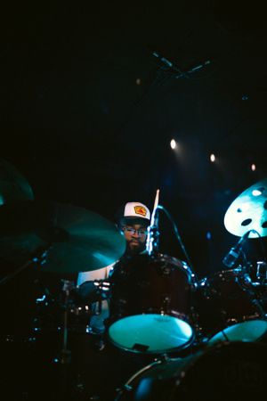 A moody low-light portrait of a drummer performing behind a drum kit.