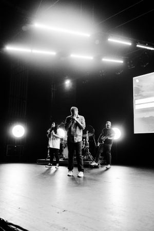 Black and white concert photo showing performers on stage with dramatic overhead lighting.