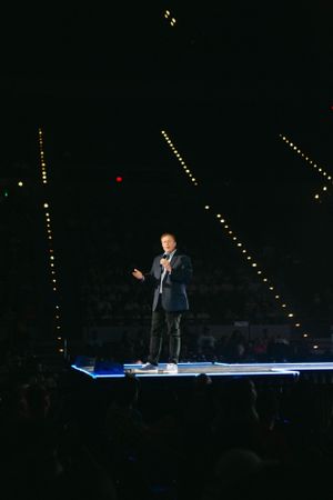 Solo performer on illuminated platform stage with decorative string lights in dark venue.