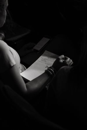 A person writing on paper in dramatic black and white lighting with bracelets visible on their wrist.