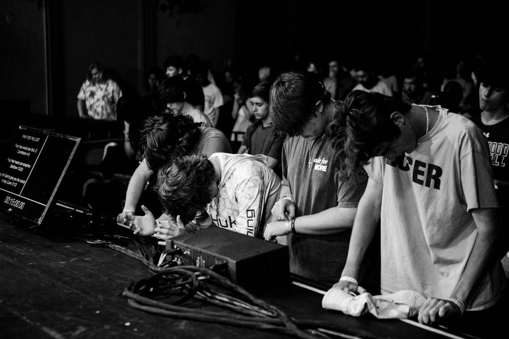 A black and white shot of people at a DJ booth during a nighttime event.