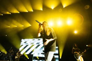 Concert performance with dramatic yellow lighting and visual effects on video wall.