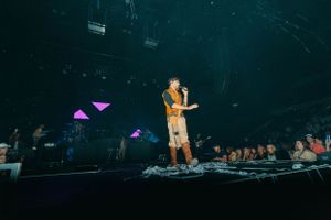 Stage performance with geometric purple lighting elements and audience silhouettes.