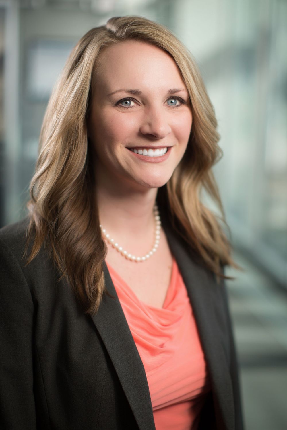 Professional businesswoman smiling in a black blazer and pearl necklace, corporate headshot photography.