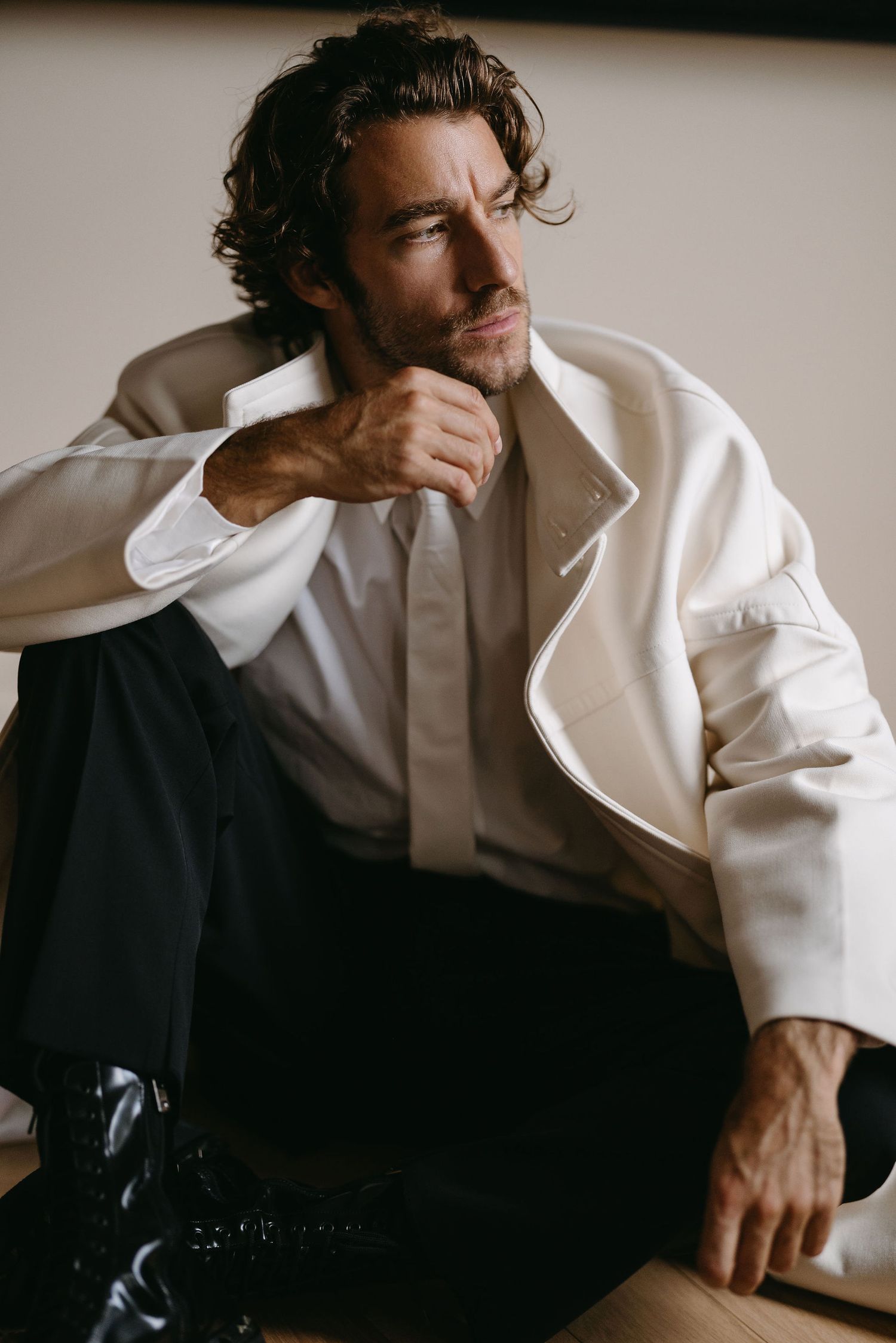 Model in white structured jacket and dark pants posing thoughtfully.
