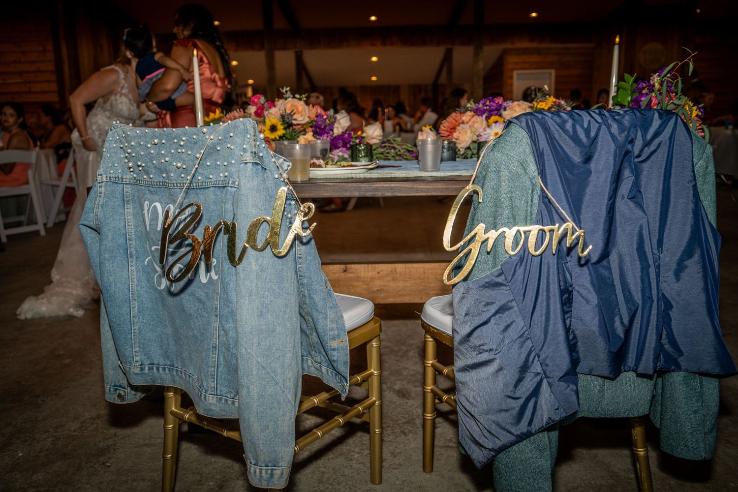 Custom denim jackets with 'Bride' and 'Groom' text hanging on wooden chairs.
