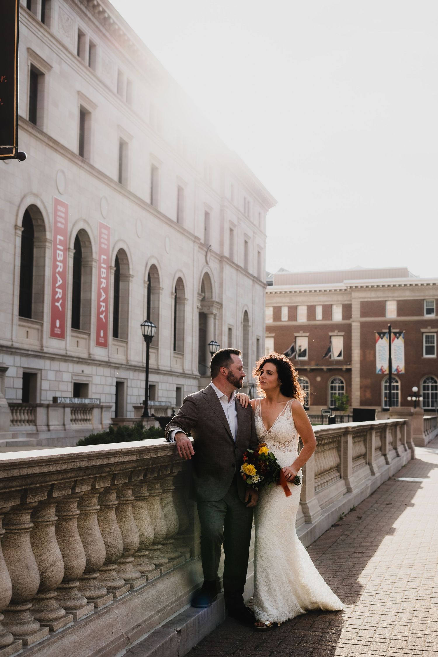 Wedding couple poses against ornate stone building with red banners and architectural details.