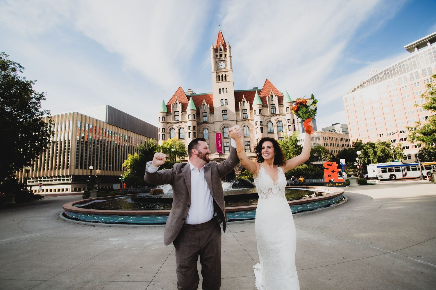 Newlyweds celebrate in front of historic red courthouse building with dramatic sky.