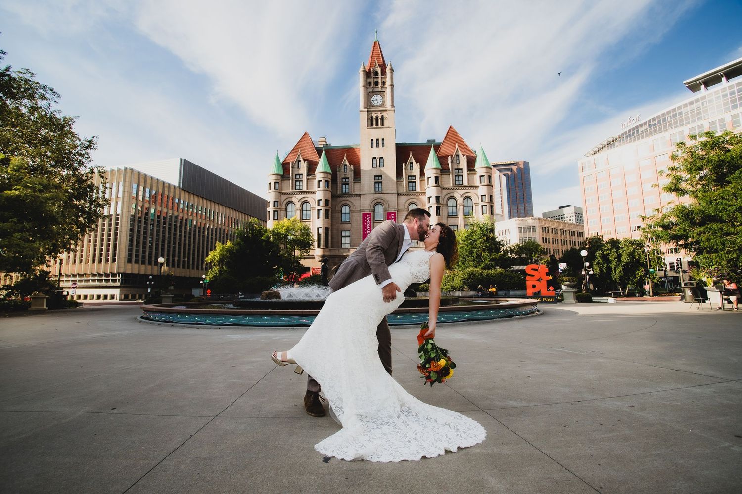 Creative wedding pose with dramatic dip in front of grand courthouse building.