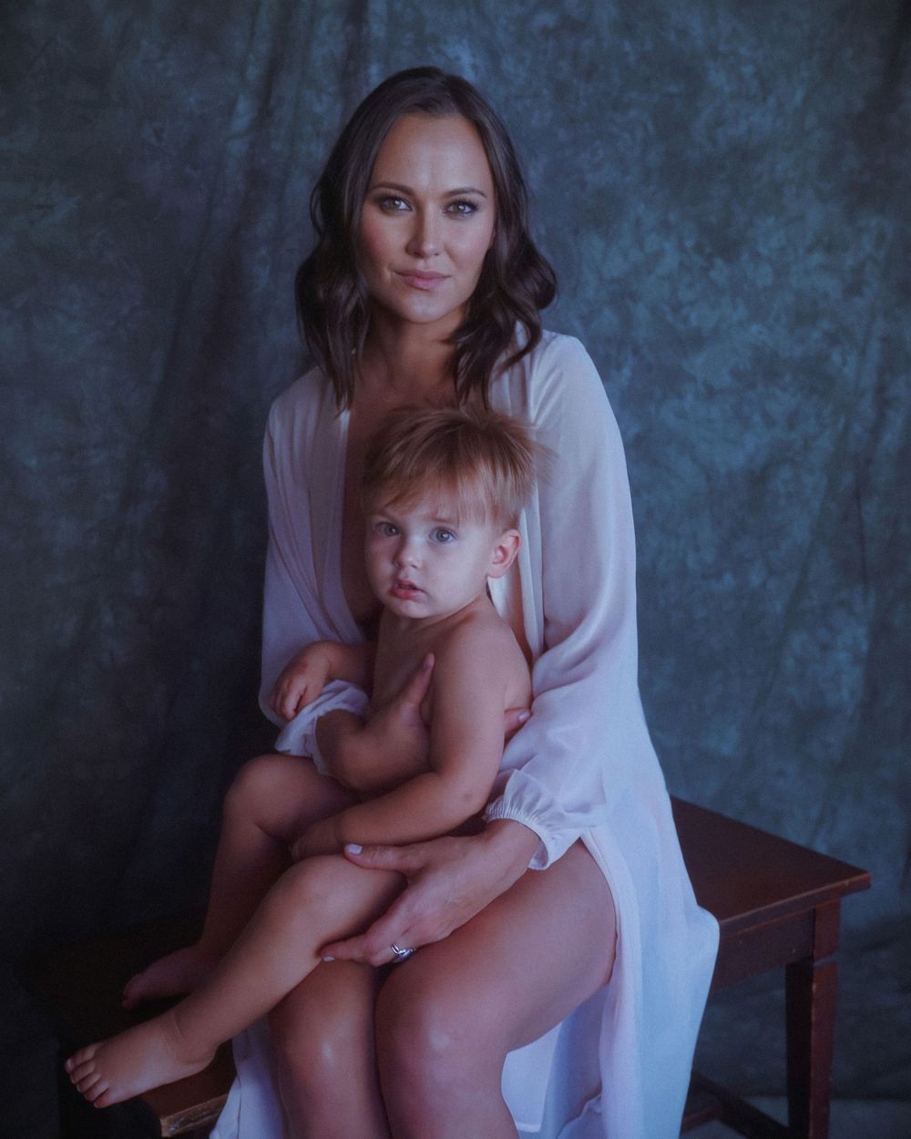 An intimate portrait of mother and child in a studio setting with soft dramatic lighting and blue backdrop.