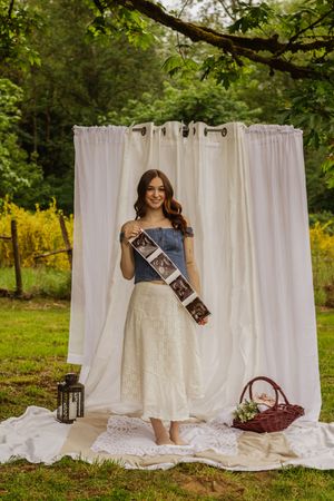 Smiling pregnant woman photographed in denim top holding ultrasound images outdoors with white curtain backdrop by Roy WA photographer