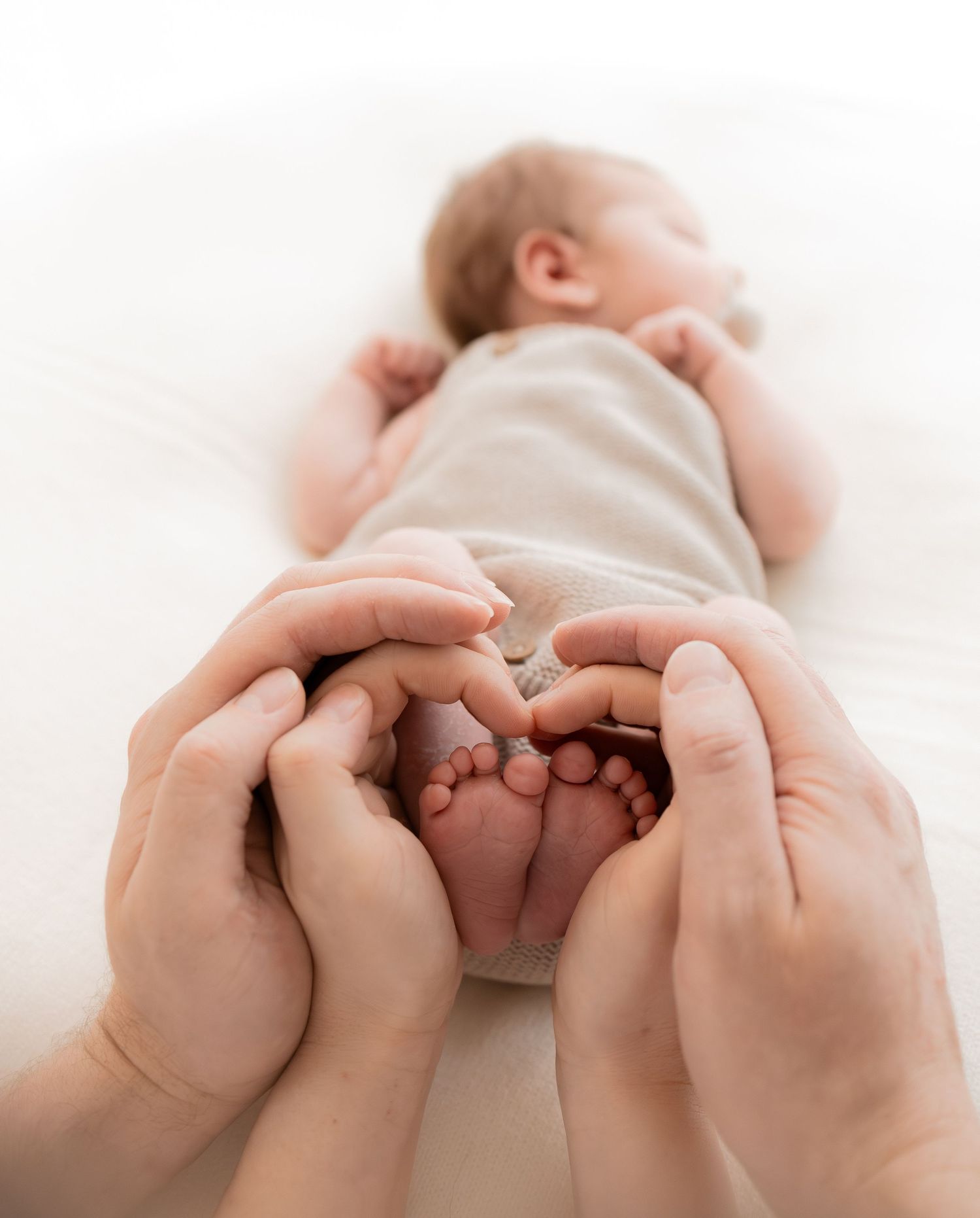 Adult hands gently cradling tiny newborn baby feet, with infant lying on white background.