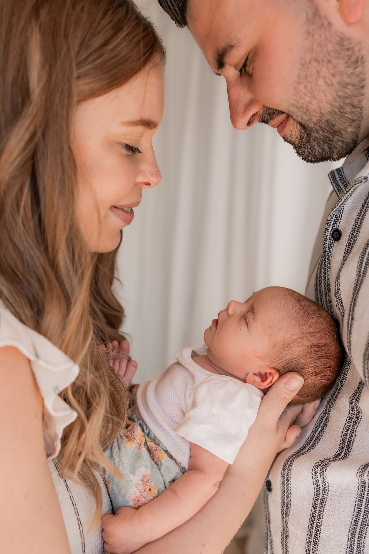 New parents lovingly gaze at their sleeping newborn baby, sharing a tender family moment together.
