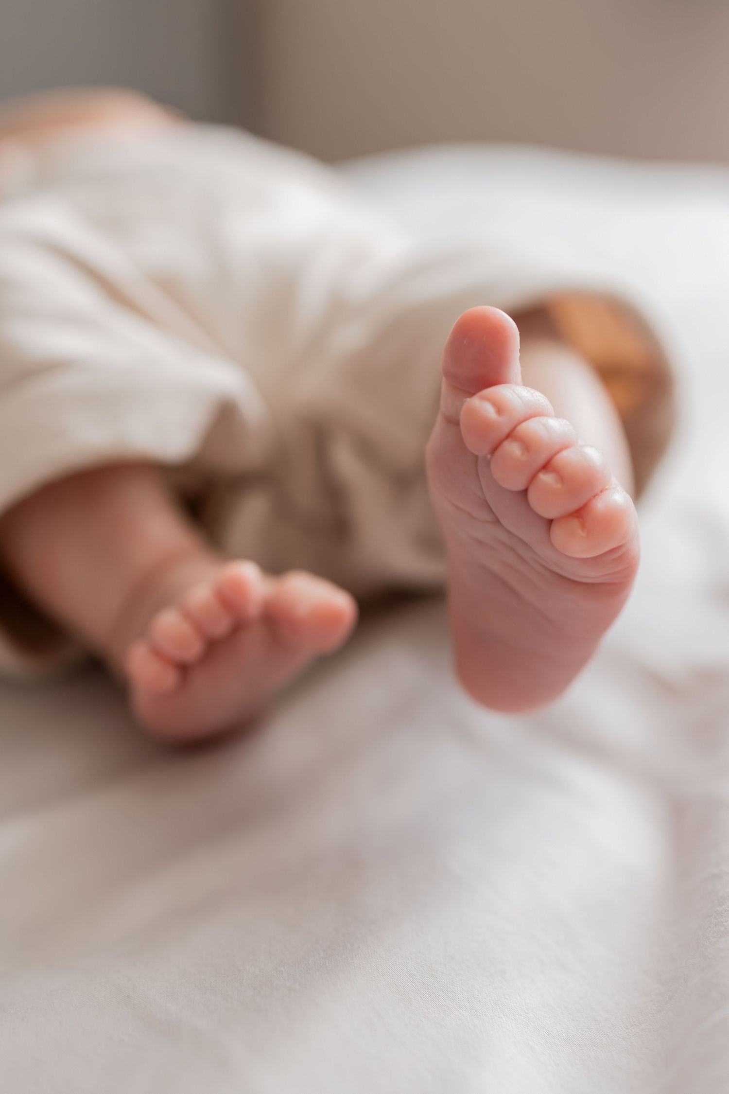 Close-up of tiny newborn baby feet resting on a soft white blanket, wearing white pants.