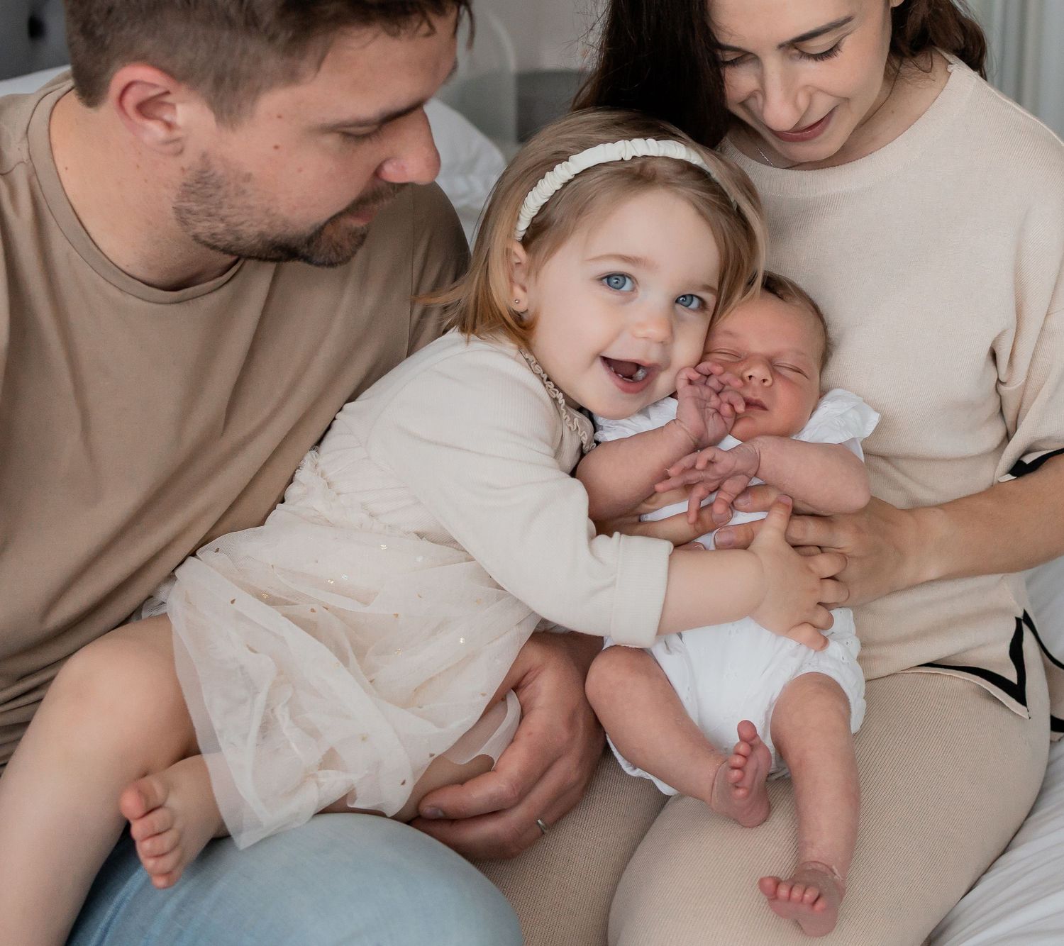 Happy family with father, mother, toddler girl, and newborn baby bonding together in a warm, cozy home setting.