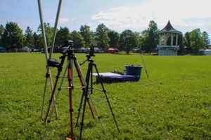 Camera tripods set up on grass field with white gazebo in background.