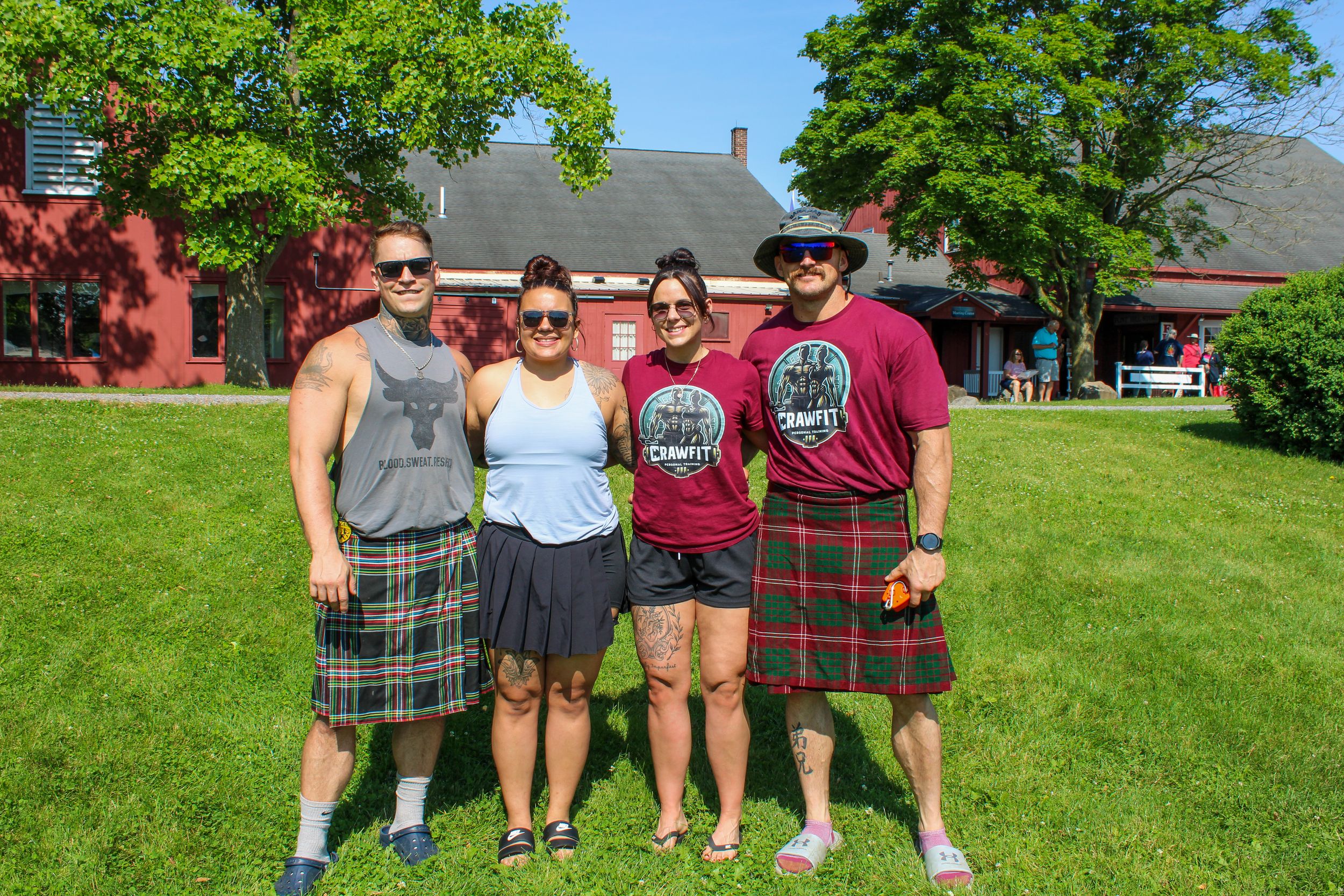 Group wearing kilts and casual attire posing on grass lawn during outdoor event.