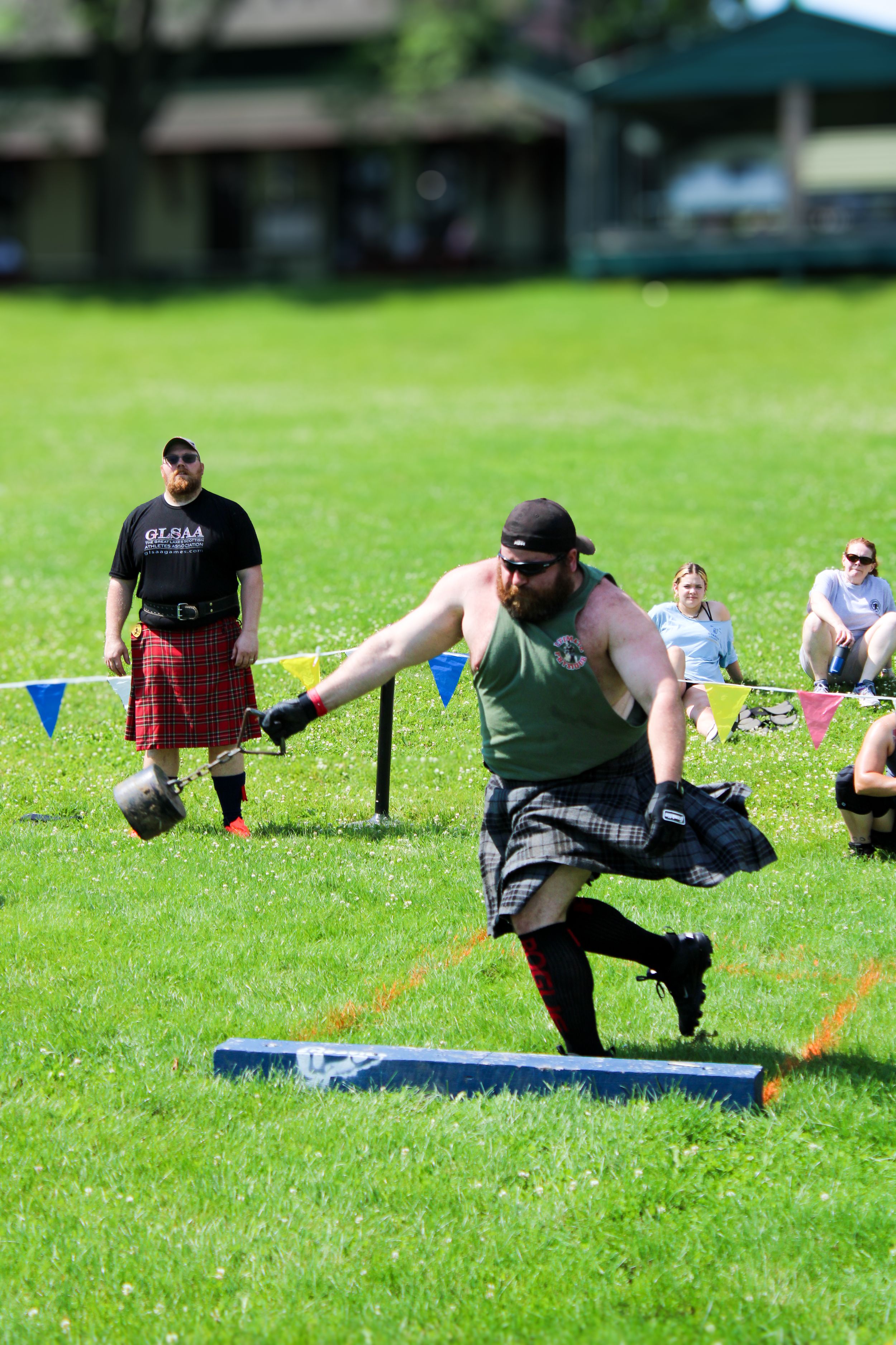 Participant in kilt competing in traditional Scottish weight throwing competition on grass field.