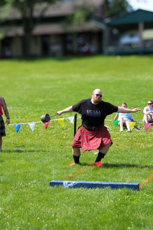 Competitor in black shirt and red kilt performing weight throw at Highland games.