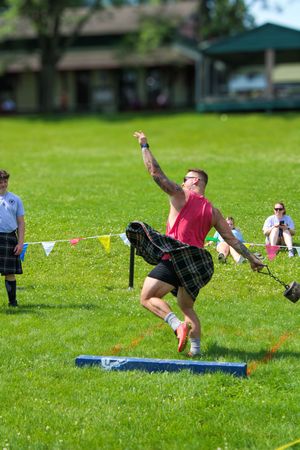 Competitor in plaid kilt performing dynamic weight throw at Highland games competition.