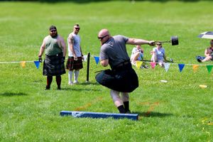 Competitor in traditional kilt performing weight throw at outdoor Highland games event.