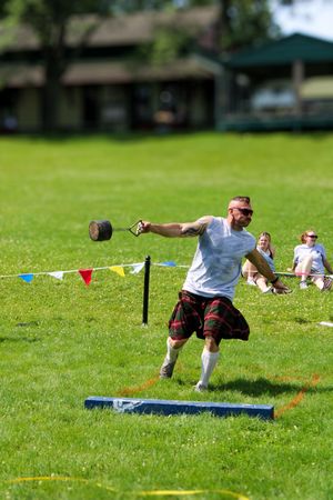 Athlete throwing weight during Scottish Highland games competition on sunny day.