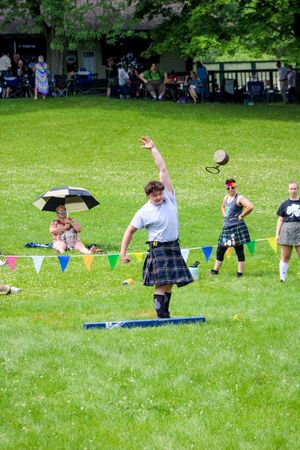 Athletes in kilts compete in traditional Scottish Highland games throwing event on a grassy field.