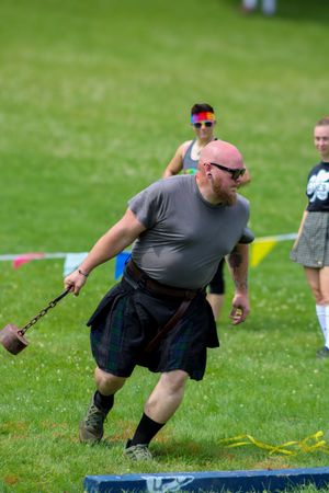 Athlete in dark kilt preparing to throw weighted chain at Highland games competition.