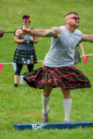 Competitors in traditional kilts perform athletic movements during Highland games competition.