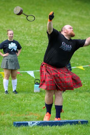 Competitor in red tartan kilt performs throwing event at Highland games.