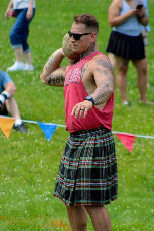 Athlete wearing pink tank top and tartan kilt participates in Highland games event.