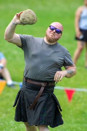 Competitor in black kilt demonstrates throwing technique during Highland games competition.