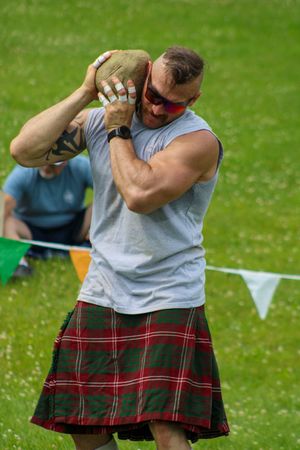 Highland games athlete in tartan kilt performs traditional throwing competition movements.