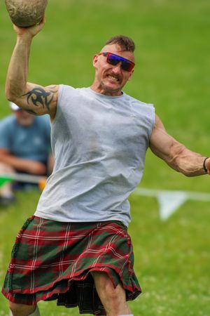 Competitor in plaid kilt demonstrates athletic form during Highland games event.