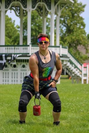 Athlete in sunglasses and athletic wear preparing for Highland Games event on grass field.