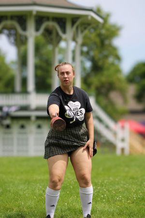Athlete in black shirt and plaid kilt preparing stance on grassy field during competition.