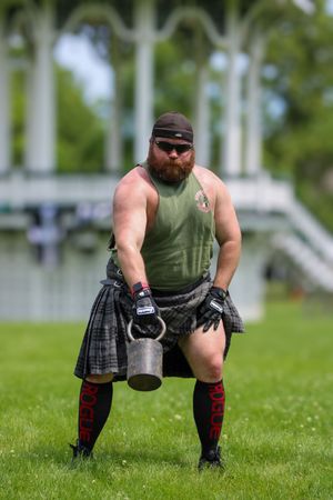 Athlete in olive green shirt and kilt practicing shot put stance at Highland Games.