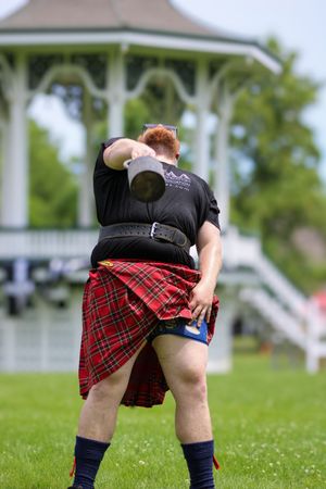 Highland Games athlete in red plaid kilt preparing for throwing event on grass field.