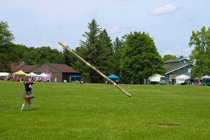 Sequence showing the progression of a caber toss attempt on a grassy competition field.