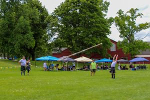 Scenic view of a Highland games field with participants and spectators gathered under shaded tents.