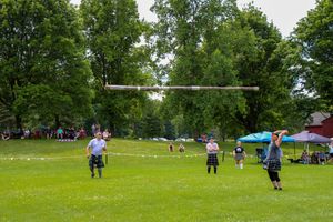 Panoramic landscape of a Highland games competition field with trees and tents in the distance.