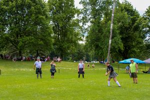 Competitors gather on a grassy field for a traditional caber toss competition at a highland games event.