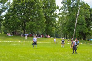 A wooden caber pole being lifted during a traditional Scottish highland games competition on a sunny day.