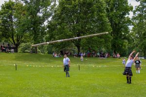 Athletes and officials prepare for caber toss event on expansive green field during highland games.