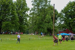 Wide view of highland games field showing caber toss competition setup with crowd gathering.