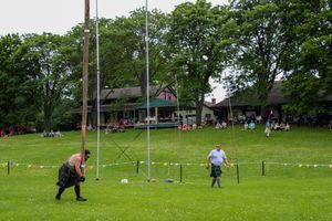 Athlete attempts caber toss during traditional Scottish highland games on grassy field.