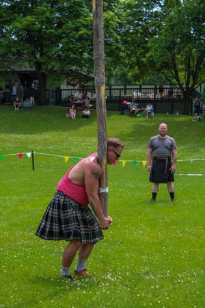 Competitors in kilts demonstrate caber toss technique at a Highland games event.