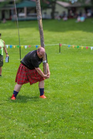 Athlete in red plaid kilt attempts caber toss at Highland games event.