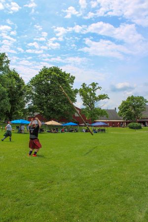 Highland games competition field under blue sky with spectators and tents in background.