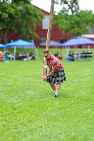 Athlete in traditional Scottish attire practices throwing technique on a grassy field during Highland Games event.